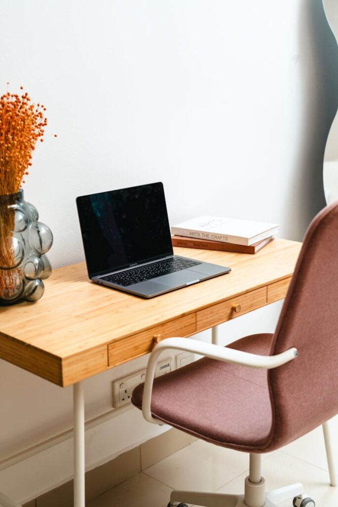 A modern home office desk with a laptop, decor, and books in a minimal setting.